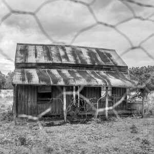 Black and white photo of an old Home looking through fencing
