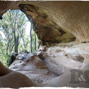 Travel photography looking out at bushland through a large sandstone cave opening